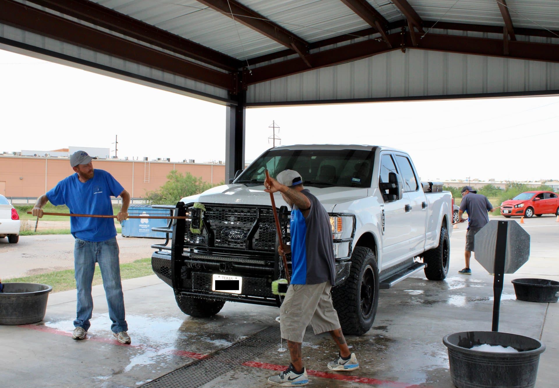 Three crew members hand-prepping a white pickup under the canopy